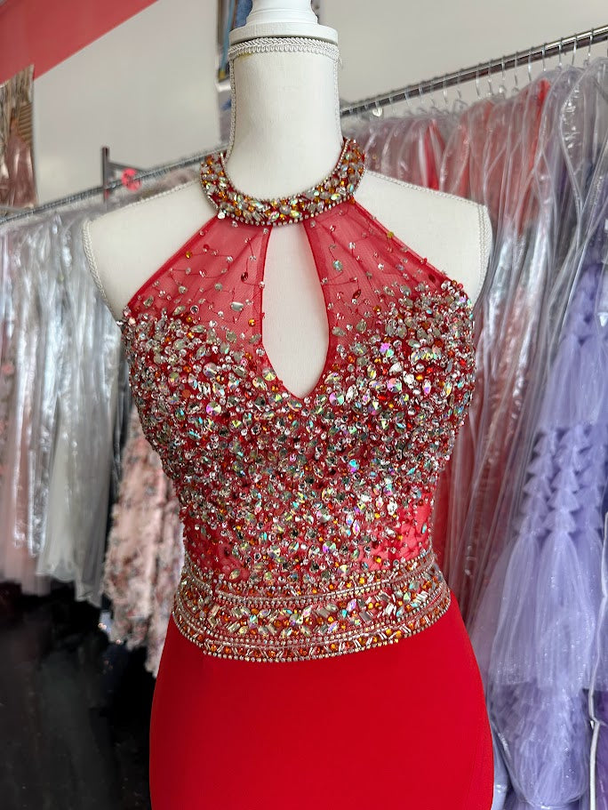 Make a striking entrance with the Jovani JVN23576, a size 2 red prom dress designed for confidence and elegance. This gown features a sheer long overlay paired with a chic choker neckline that frames the plunging neckline beautifully. A daring slit adds both allure and ease of movement, perfect for pageants or formal events. Crafted to enhance your silhouette, this dress balances bold design with refined sophistication.

Stunning halter form fitting dress features a sexy thigh high slit and crystal embellis
