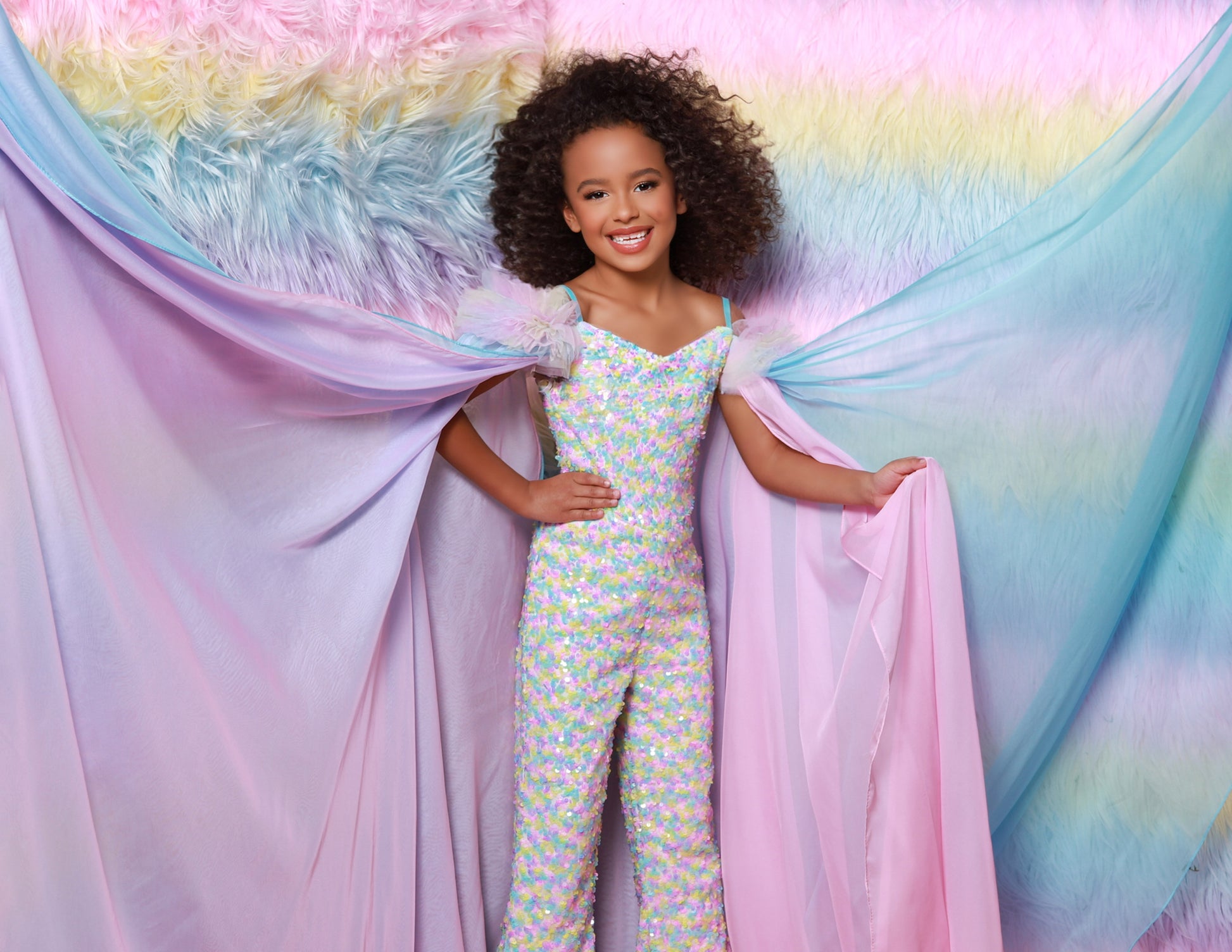 The Sugar Kayne C341 Jumpsuit is the perfect choice for your little princess. This fashionable, comfortable outfit features an all-over sequin design, ruffle sleeves and matching cape for a unique look. Perfect for clinics, pageants and any special occasion. 