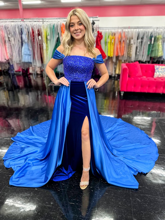 This Johnathan Kayne 2725 gown combines luxurious velvet with elegant satin details for a striking pageant look. The fitted silhouette features a straight neckline and a crystal-beaded bodice that adds refined sparkle. Detachable off-the-shoulder satin sleeves offer versatile styling, while the long satin overskirt and corset lace-up back with crystal tassels enhance both drama and fit. A tasteful slit completes this sophisticated design, perfect for making a memorable impression.

Size: 4&nbsp;

Color: Roy