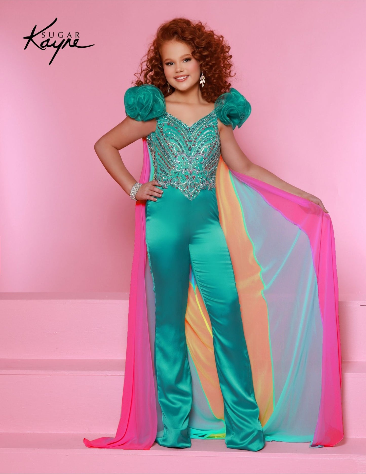 The Sugar Kayne C335 Girls Two Piece Fun Fashion Jumpsuit features a beaded bodice, a detachable cape, and a stylish, comfortable fit. Perfect for pageants, the outfit is sure to make your child look her best. Step into a whirlwind of whimsy with this Crepe Back Satin Jumpsuit. The beaded bodice, ruffle sleeves, and detachable colorful chiffon cape make every day a playful and stylish adventure.