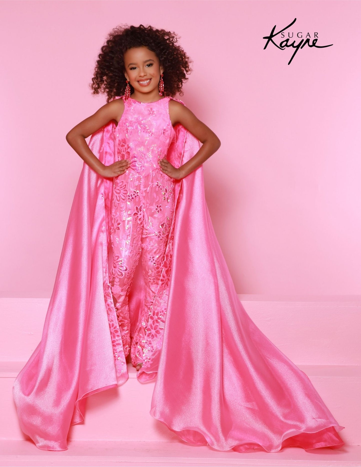 This beautiful Sugar Kayne C337 pageant jumpsuit makes the perfect statement for special events. It features a stunning sequin mesh with shimmer organza cape for a magical look. Perfect for formal functions, the durable fabric and flattering design guarantee a timeless look. Become a shimmer superstar and rock the stage in our Sequin Mesh and Shimmer Organza Jumpsuit. The detachable dazzling cape adds a super fun touch!