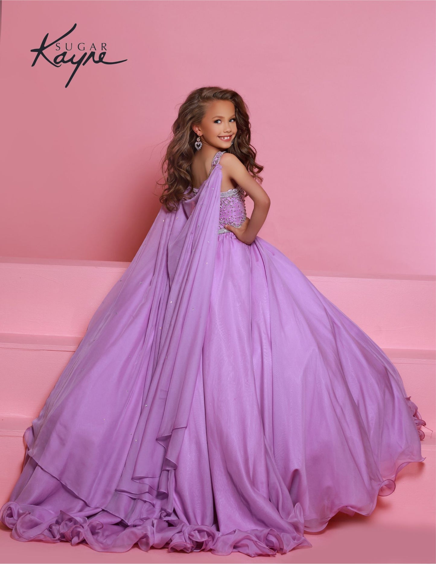 Sugar Kayne C329 Lilac Pageant Dress features a chiffon skirt, semi sweetheart neckline encrusted with rhinestones and wide straps with a cape.