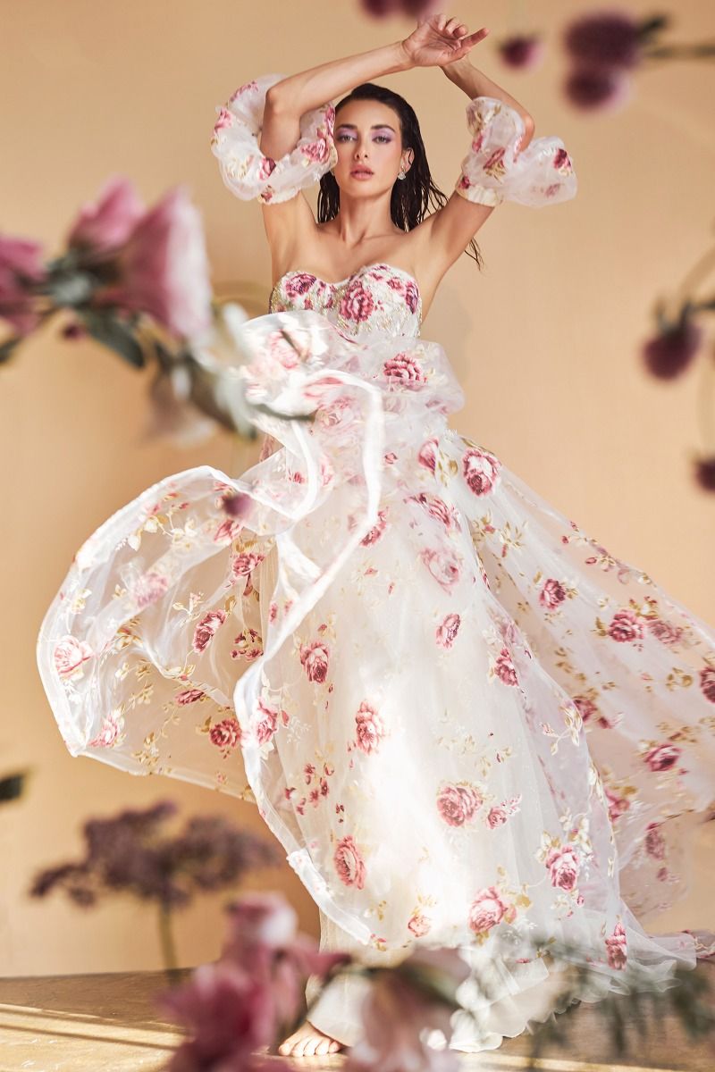 Elevate your formal attire with the Andrea & Leo Couture A1133 Floral Print A Line Prom Dress. The crystal embellished bodice adds a touch of glamour to the classic floral print, while the puff sleeves and sheer corset exude elegance. Perfect for any special occasion, this dress combines style and sophistication in one stunning design. This strapless organza peony print ball gown is a breathtaking and romantic choice for any fairytale garden. 