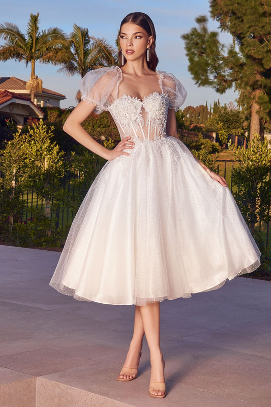 Look and feel like royalty on your special day with the Ladivine CD0187W Short Tea Length Shimmer White Dress. Constructed of sheer corset lace and featuring puff sleeve detailing, this beautiful A-line gown is sure to make you shine. The glitter tulle skirt and subtle glitter print embellishment add just the right sparkle. Each step you take will be truly magical!  Sizes: XS-3X  Colors: Off White