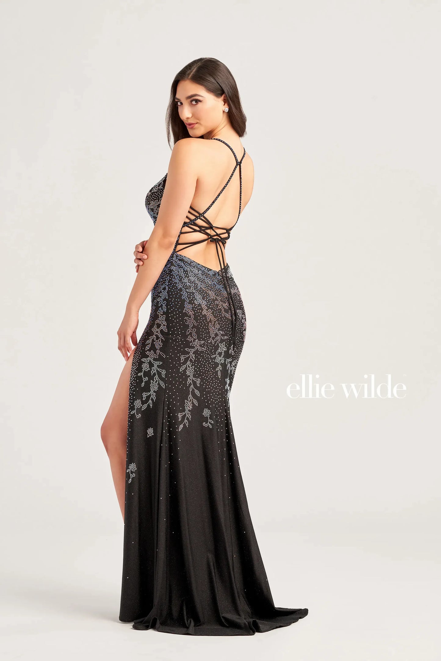 Expertly crafted, the Ellie Wilde EW35061 is a stunning backless corset prom dress. The fitted silhouette and shimmer jersey fabric create a flattering look, while the crystal embellishments and V-neckline add a touch of glamour. The high slit adds a daring element to this elegant gown.  Sizes: 0-16  Colors: EMERALD, ROYAL BLUE, BLACK GALAXY