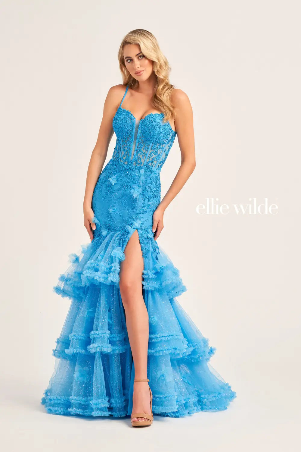 Be the star of the night in this Ellie Wilde EW35050 prom dress. The sheer lace corset with 3D dimensional appliques creates a flattering silhouette while the Tiered Tulle pleated ruffle layered trumpet skirt features a slit and shimmer fabric add a touch of glamour. The pleated mermaid skirt and slit offer both elegance and comfort.  Sizes: 00-16  Colors: OCEAN BLUE, LIGHT BLUE, HOT PINK