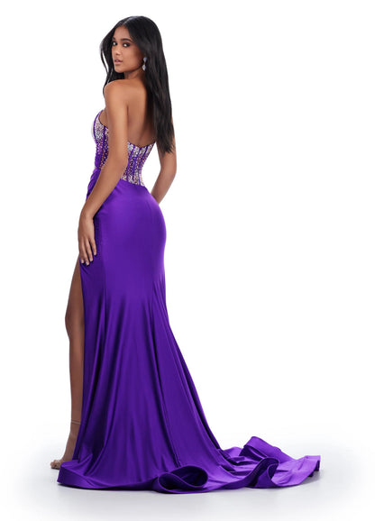 The Ashley Lauren 11617 Evening Gown is crafted from sheer fabric with a one shoulder design adorned with delicate crystal embroidery. The fitted silhouette features a corset bodice with a maxi slit and long train with a voluminous skirt. Perfect for prom, pageants, and formal events. Elegance with a twist! This one shoulder jersey gown features a stunning beaded corset bustier for an added touch of glam.  COLORS: Purple, Magenta, Peacock, Black Sizes: 00-24
