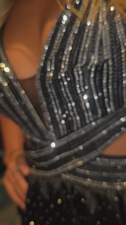 Nina Canacci's 9200 is a show-stopping pageant gown that combines elegance with contemporary flair. The crystal-layered jersey skirt features intricate micro crystal embellishments that catch light beautifully, while strategic side cutouts add modern sophistication. A dramatic maxi slit and flowing train create movement and grandeur, making this dress ideal for prom, pageants, and formal competitions. The jersey construction ensures comfortable wear throughout the evening while maintaining a polished silhou
