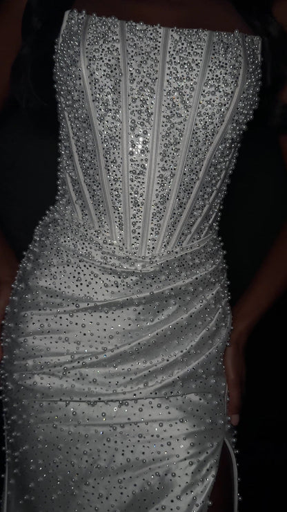 ASHLEYlauren Style 12356 is a fully beaded evening gown that commands attention with its fitted silhouette and strapless neckline.&nbsp; Ashley Lauren 12356 The expertly contoured bodice features vertical beadwork that accentuates the waist and elongates the figure, while a sweeping train with slit adds dramatic movement. Crafted from jersey fabric with pearl corset bustier detailing, this gown delivers high-impact sparkle from every angle. Ideal for pageants, red carpet events, prom, galas, and special occ