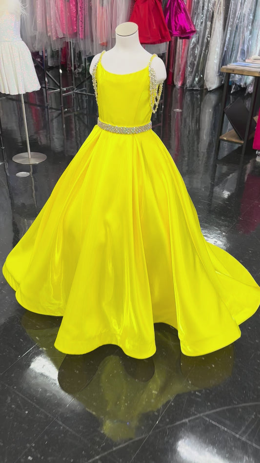 Ashley Lauren 8333, a stunning satin A-line gown designed for young competitors. This sophisticated dress features shimmering fabric that catches the light beautifully, complemented by elegant crystal-embellished off-the-shoulder straps that frame the neckline with glamour. The coordinating belt cinches the waist for a polished silhouette, while practical hidden pockets add functionality without compromising style. The flowing A-line skirt creates graceful movement on stage, ensuring your daughter commands 