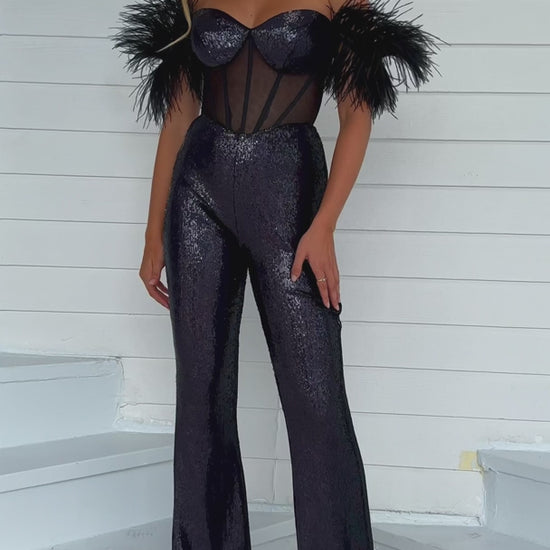 The Ava Presley 39577 Long Sequin Jumpsuit is designed to make you stand out at any formal event. The intricate sequin detailing and sheer corset add an alluring touch, while the feather off-the-shoulder sleeves add a touch of elegance. Perfect for pageants or other formal occasions.  Sizes: 00-16  Colors: Black/AB, Iridescent White, Light Blue