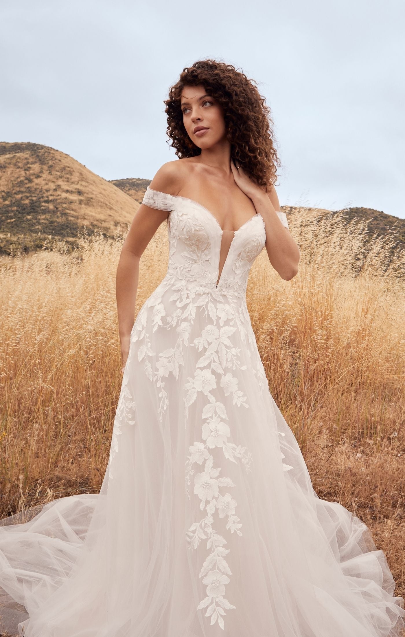 Casablanca Beloved BL433 A-Line Floral Lace Deep V-Neck Off The Shoulder Tulle Train Wedding Gown. Penny’s A-line silhouette defines her feminine form, perfectly subtle yet flattering on any size and shape. A symphony of floral lace appliques flow from her bodice, trailing down into her flattering A-line skirt