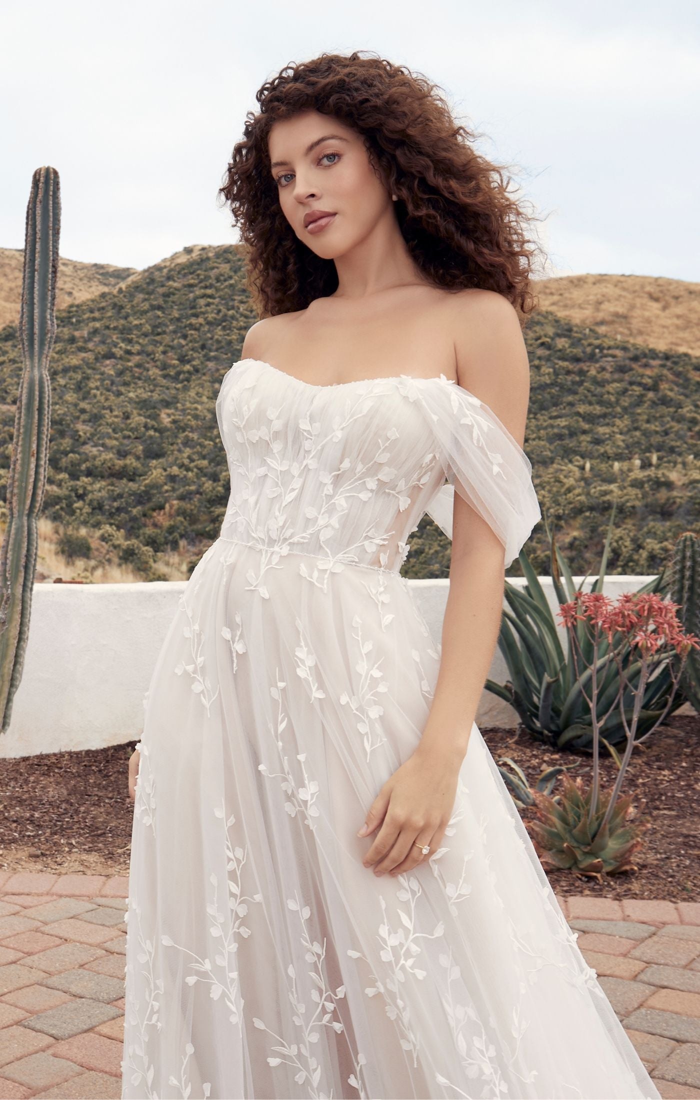 Casablanca Beloved A-Line Off The Shoulder Sweetheart Neckline Tulle Train Wedding Gown. Indulge in the ethereal elegance of Style BL428 Calico, a gown designed to transport you to a world of enchantment on your special day. The A-line silhouette and modified strapless sweetheart bodice of Calico exude timeless beauty and sophistication. The detachable off-the-shoulder sleeves add versatility, allowing you to create different looks to suit your style and mood.