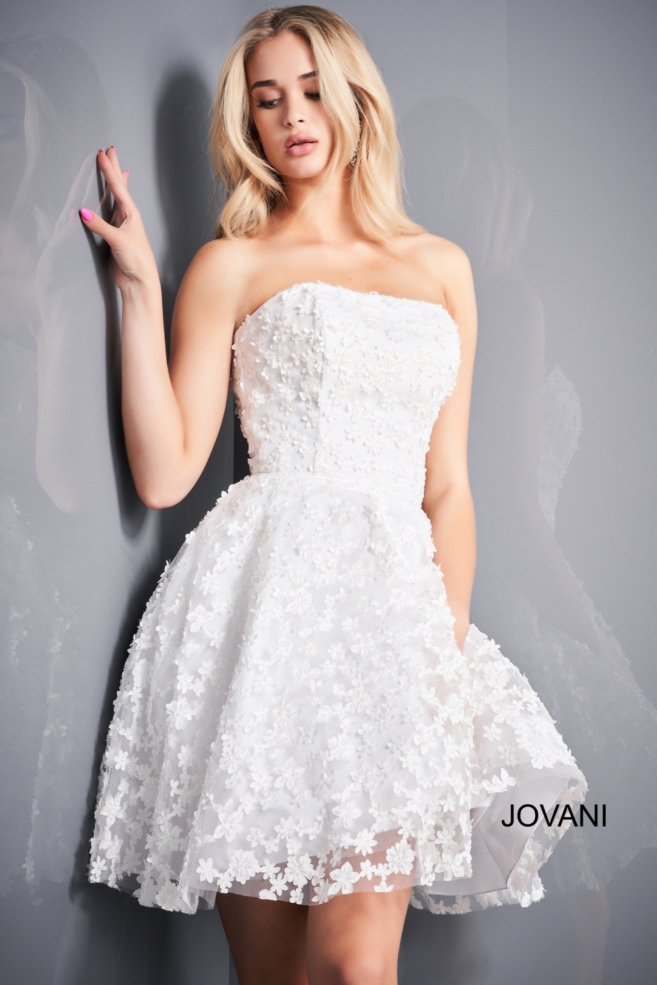 Jovani 02564 is a short Fit & Flare cocktail dress perfect for homecoming, wedding reception, prom & More! Strapless straight neckline with a fitted bodice covered in 3D floral Appliques. Pockets in the flared skirt. Corset Lace up back.  Available Sizes: 00,0,2,4,6,8,10,12,14,16,18,20,22,24  Available Colors: White