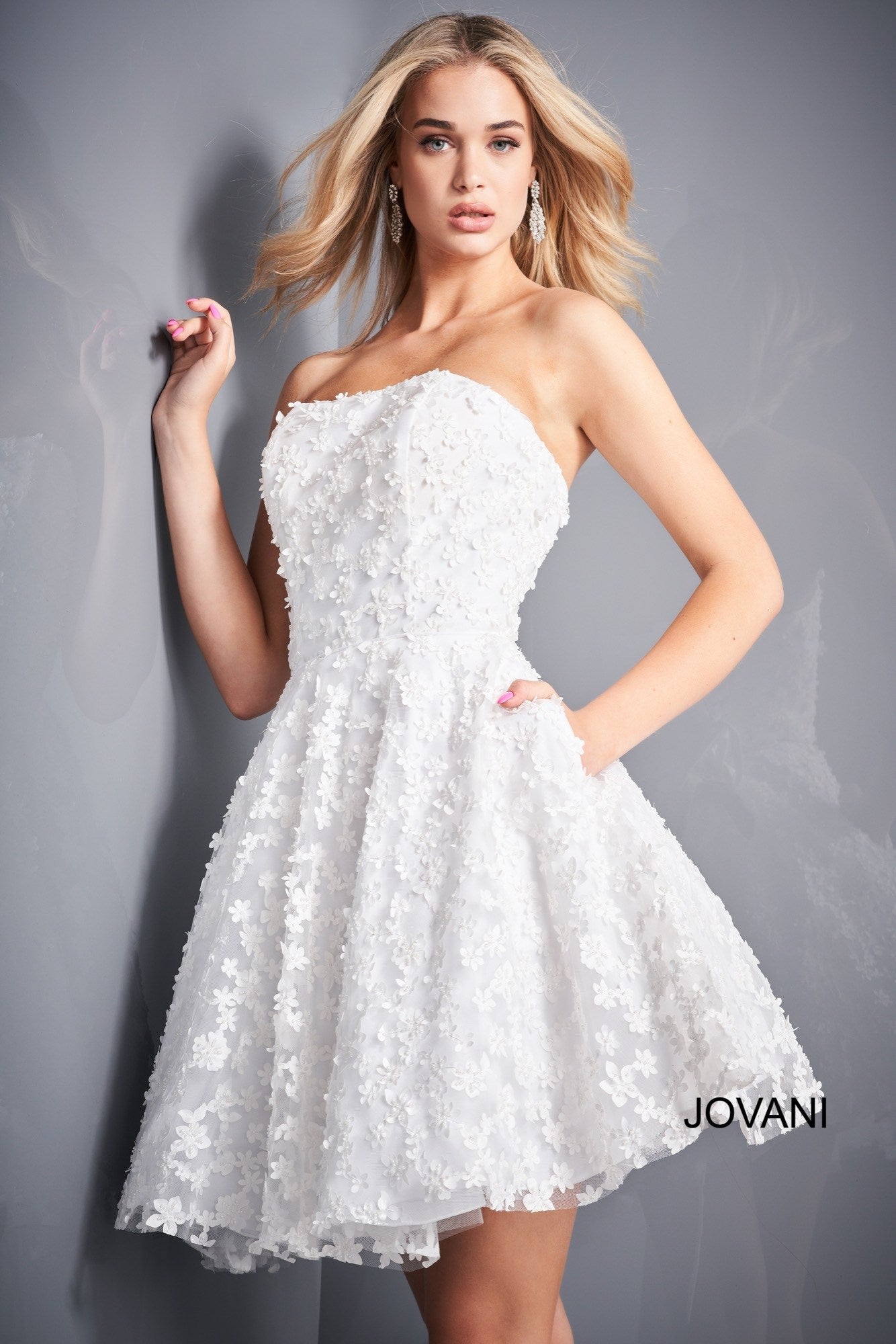 Jovani 02564 is a short Fit & Flare cocktail dress perfect for homecoming, wedding reception, prom & More! Strapless straight neckline with a fitted bodice covered in 3D floral Appliques. Pockets in the flared skirt. Corset Lace up back.  Available Sizes: 00,0,2,4,6,8,10,12,14,16,18,20,22,24  Available Colors: White