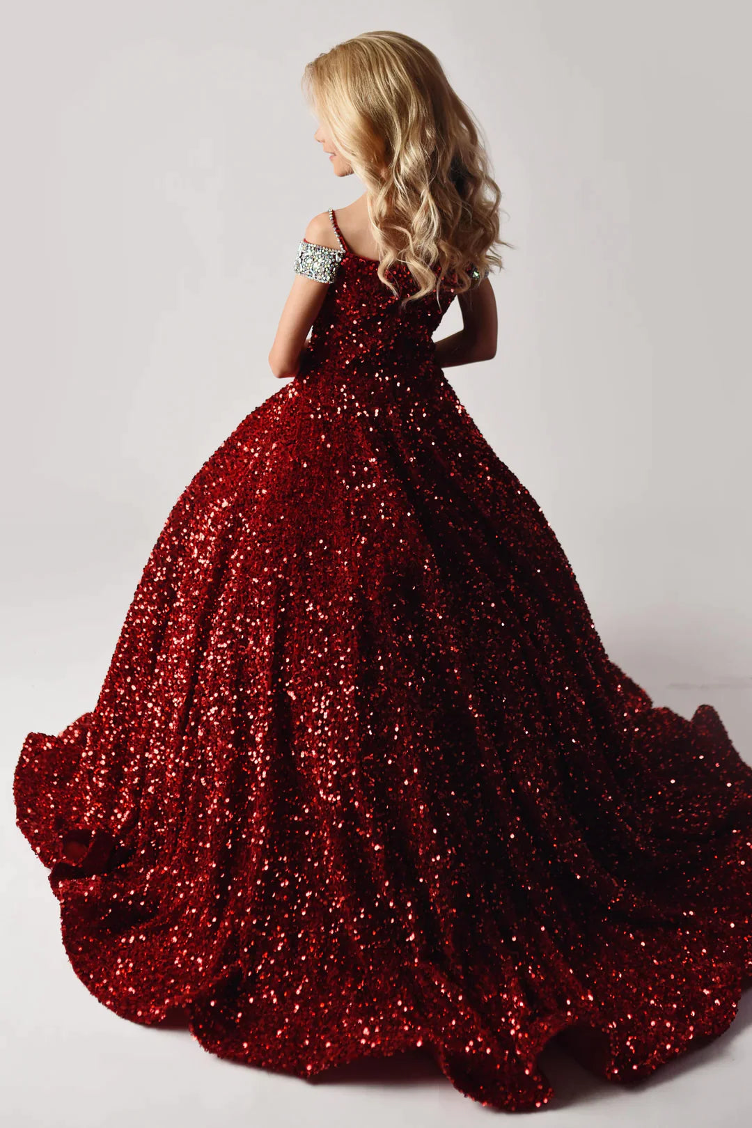 Ava Presley 27733 delivers a timeless look with its long velvet sequin ballgown. Crafted with an off-the-shoulder silhouette and beautiful crystal straps, this piece is sure to make her stand out. 100% polyester construction guarantees long-lasting wear.  Sizes: 2-16  Colors: Red, Royal, Iridescent White, Iridescent Pink, Iridescent Light Blue
