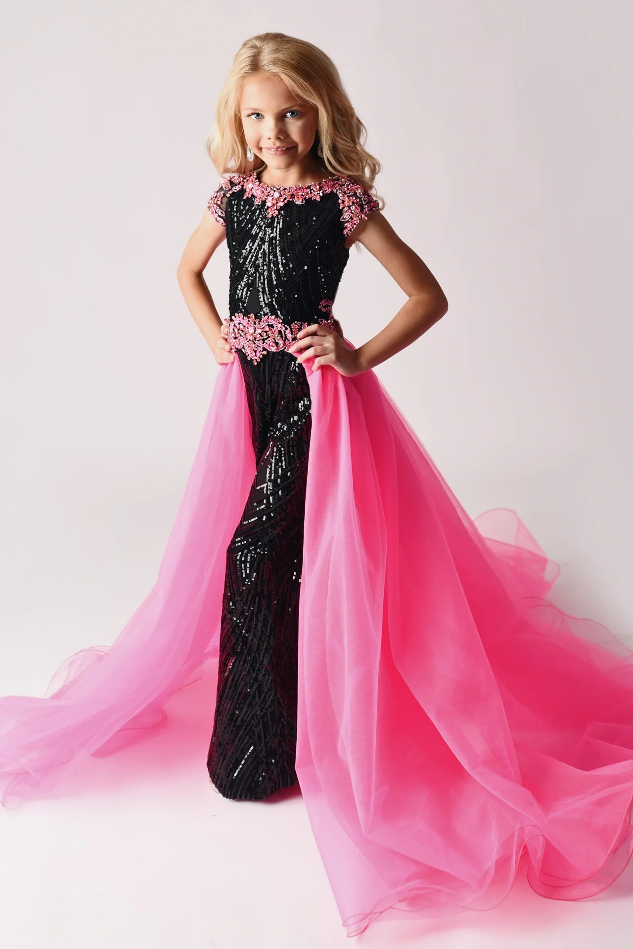 The Ava Presley 38026 Long Sequin Girls Jumpsuit features an exquisite beaded sleeve and overskirt design and is crafted of a fun and fashionable sequin fabric. It is designed to give your little girl maximum comfort, while turning up the wow factor.  Size: 2-16  Colors: Black/Hot Pink, Black/Light Blue