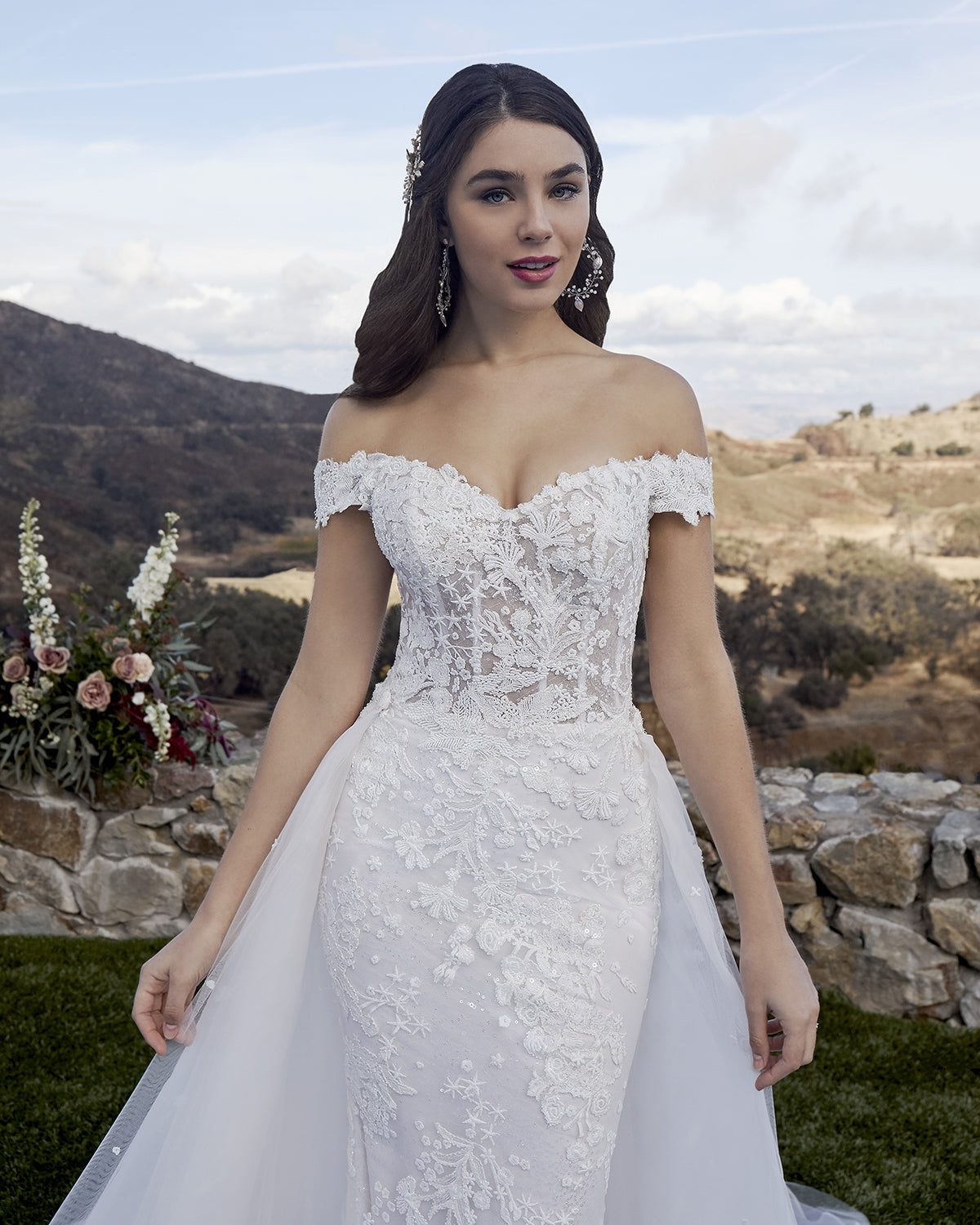Casablanca Bridal 2419 MCKENZIE Wedding Dress Overskirt Bridal Gown off the shoulder  Beach wedding dress glam rises to a whole new level of beauty with Style 2419 McKenzie by Casablanca Bridal. Beaded lace appliques take shape as subtle stars and flowing botanicals, sitting delicately atop sequined tulle that catches the sunlight at every angle. A classic fit-and-flare silhouette hugs the natural shape of the body comfortably, while a removable organza skirt attachment with matching lace appliques, 