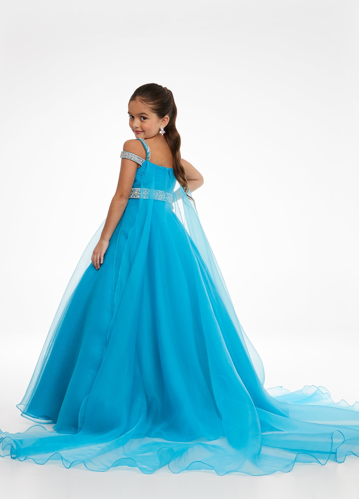 Ashley Lauren Kids 8094 Long off the shoulder A Line Pageant Ball Gown Pageant Dress We are obsessed with this kids evening gown! This organza ball gown features crystal encrusted straps giving way to a ruched bustier. The same crystal detail accents the elegant beaded belt. The look is completed with an A-Line skirt and attached organza cape. Ruched Bustier Crystal Strap &amp; Belt Organza Ball Gown Skirt Organza Cape Available Sizes: 4-14 Available Colors: Neon Orange, Orchid, Hot Pink, Turquoise, Ivory