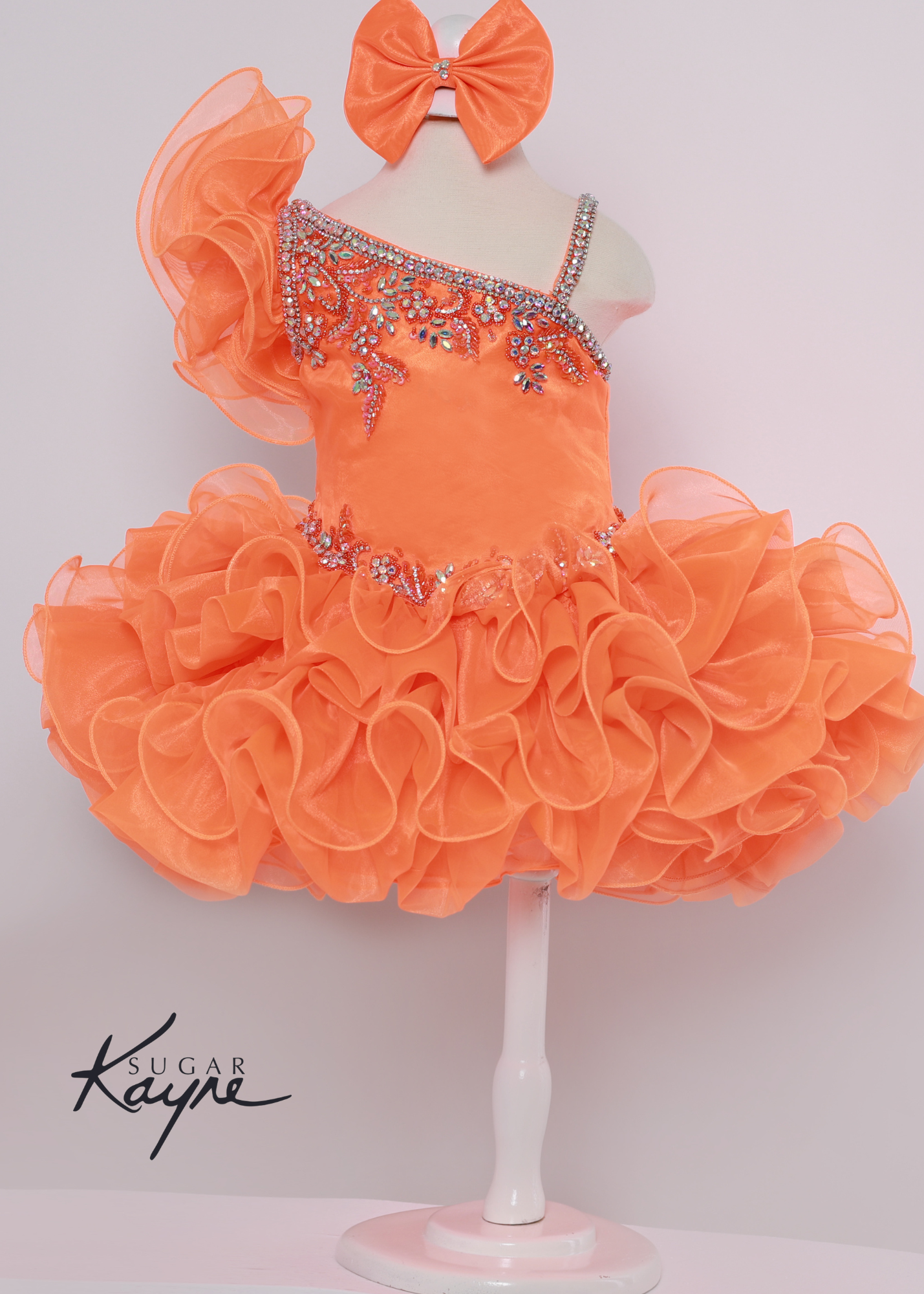Sugar Kayne C215 Girls Short Cupcake Ruffle One Shoulder Pageant Dress Bow Corset Have your little cupcake bring on all the charm in this stunning organza gown. The corset back is the perfect addition as the little one grows!  Colors: Kiwi, Neon Orange, White  Sizes: 0M, 12M, 18M, 24M, 2T, 3T, 4T, 5T, 6M, 6T  Fabric Organza, Satin Lining