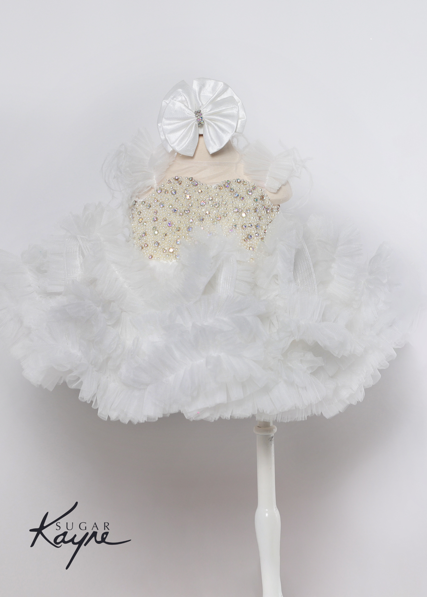 Sugar Kayne C217 Short Pleated Ruffle Cupcake Pageant Dress AB Crystal Pearl Bodice Corset. Have your little cupcake bring on all the charm in this stunning mesh gown accented with pearls. The corset back is the perfect addition as the little one grows!  Colors: White  Sizes: 0M, 12M, 18M, 24M, 2T, 3T, 4T, 5T, 6M, 6T  Fabric Mesh, Satin Lining