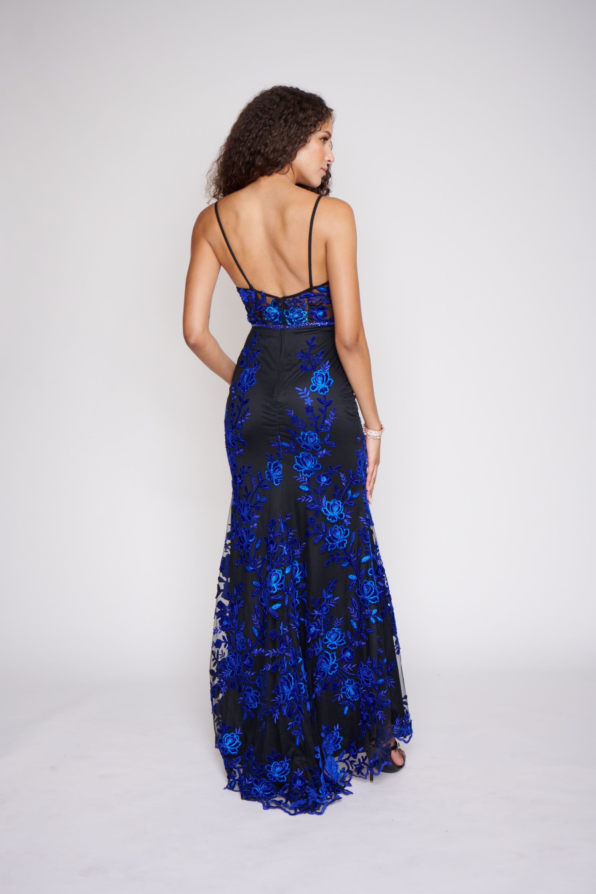 Nina Canacci 2240 Black Royal Long Prom Dress Evening Gown Fit and Flare Floral Lace Dress.  This dress is black with royal blue applique lace through out the dress.  It has a v neckline with sheer panel and a sheer lace back.  The long skirt is a fit and flare style. 