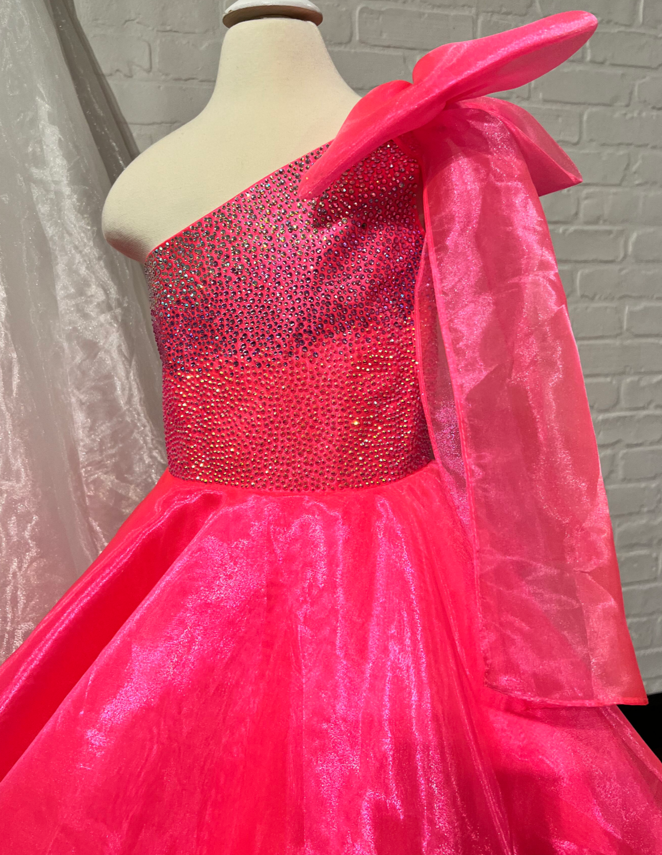Sugar Kayne C310 Girls and Preteens One Shoulder Bow A Line Shimmer Pageant Dress Crystal Gown  Go ahead and take a BOW in this lovely one-shoulder organza ballgown. The ombre beaded bodice brings all the dazzle!  Colors: Orange, Yellow, Blue, White, Neon Pink