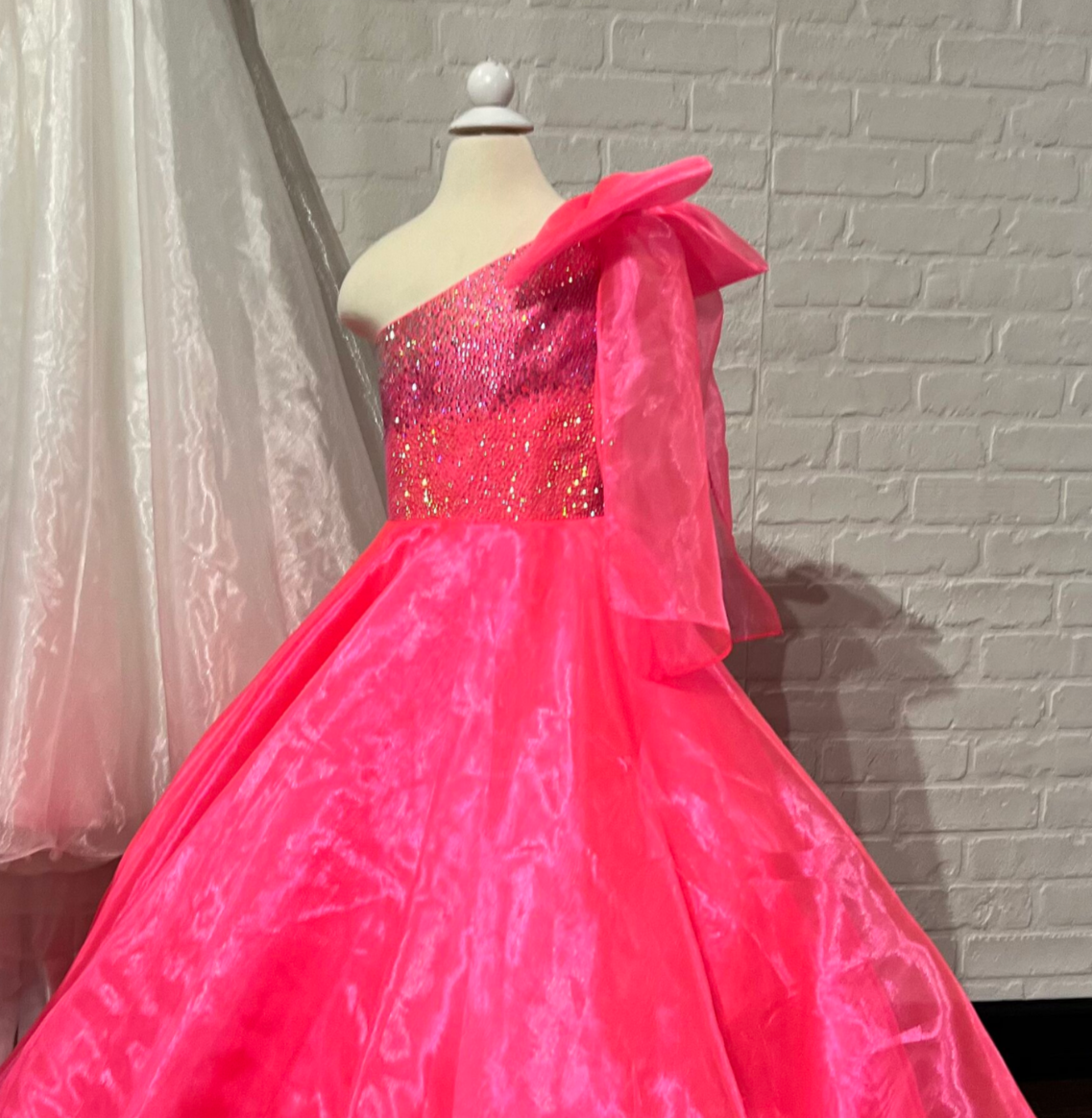 Sugar Kayne C310 Girls and Preteens One Shoulder bodice with a Bow on the shoulder A Line Shimmer Pageant Dress Crystal Gown&nbsp;
Go ahead and take a BOW in this lovely one-shoulder organza ballgown. The ombre beaded bodice brings all the dazzle!

Colors:
Orange, Yellow, Blue, White, Neon Pink

Sizes:
2, 4, 6, 8, 10, 12, 14, 16

Fabric Organza, Mesh, Satin Lining

(Sizes 2-6 do not have bust cups, Sizes 8-16 will have preteen size bust cups)