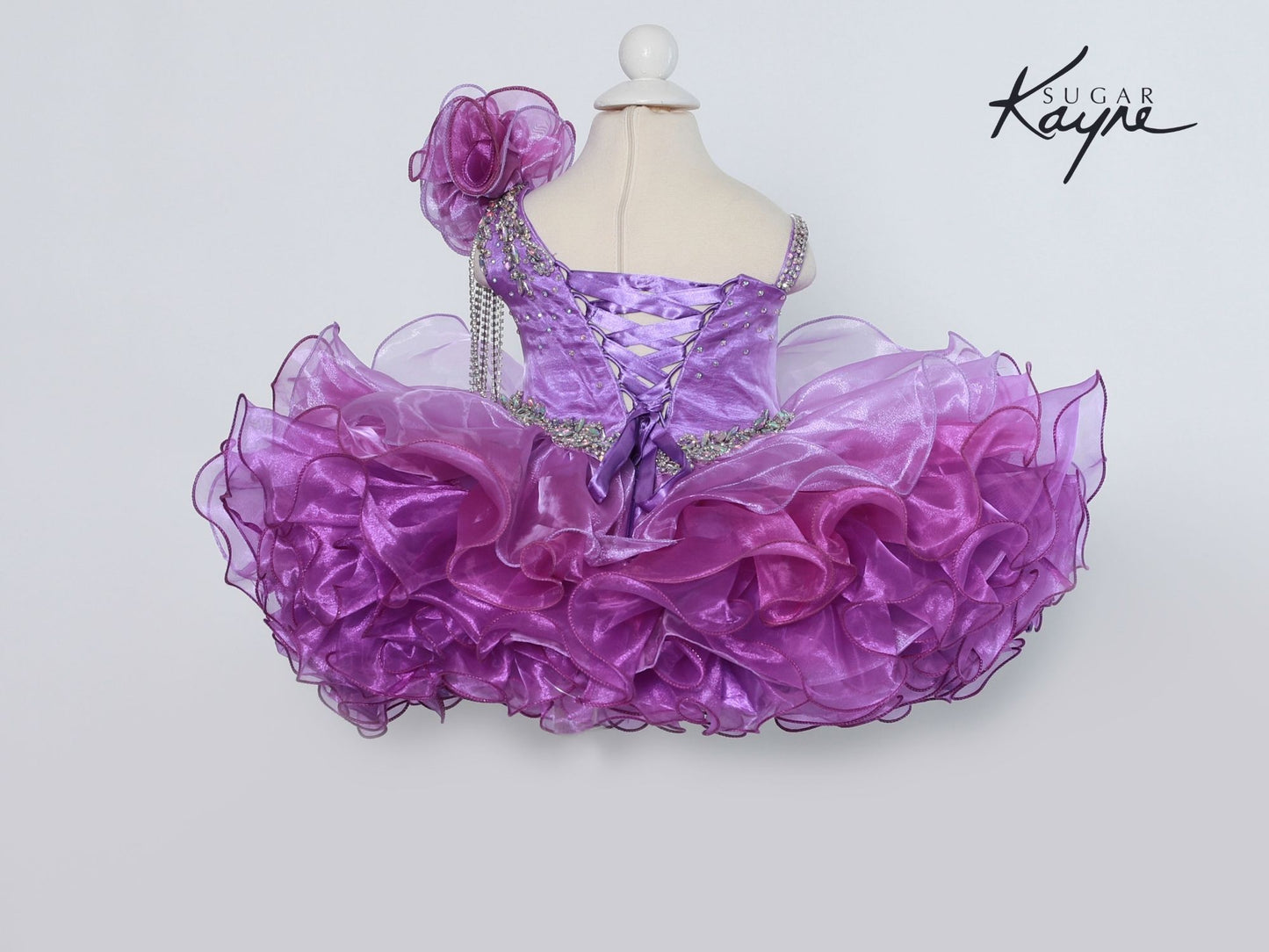 Sugar Kayne C206 One Shoulder Ombre Cupcake Pageant Dress Rhinestone Tassel Formal Gown One Shoulder with an organza embellishments and rhinestone fringe. Corset back lace up. Ombre color shift.  sizes: 0M, 6M, 12M, 18M, 24M, 2T, 3T, 4T, 5T, 6T  Colors: Sunset, Iris