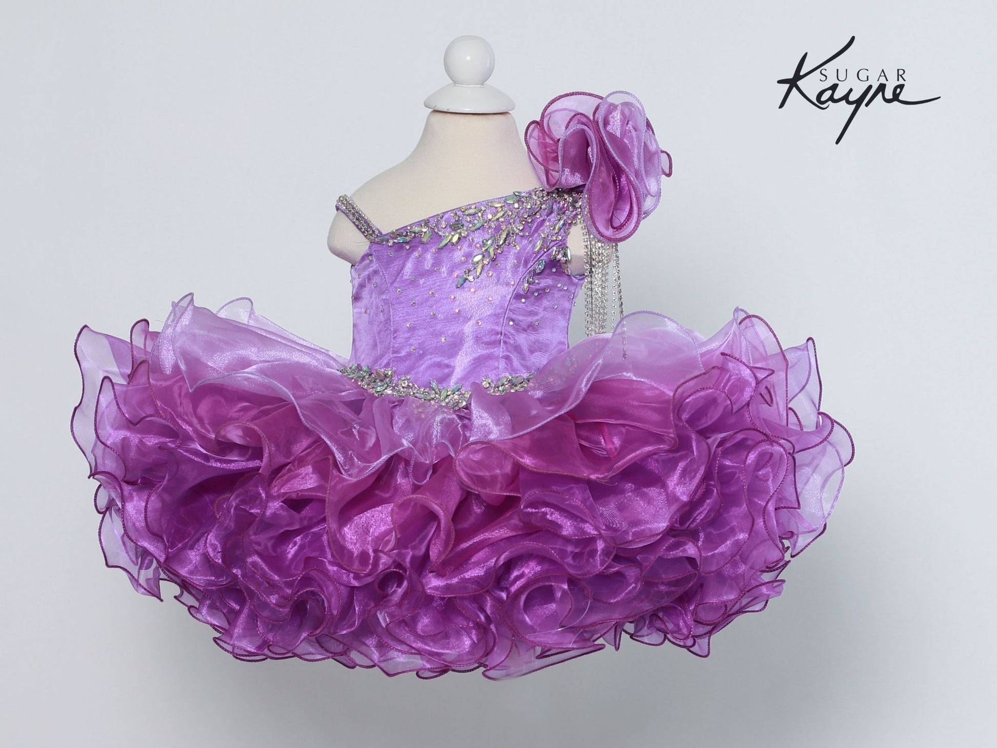 Sugar Kayne C206 One Shoulder Ombre Cupcake Pageant Dress Rhinestone Tassel Formal Gown One Shoulder with an organza embellishments and rhinestone fringe. Corset back lace up. Ombre color shift.  sizes: 0M, 6M, 12M, 18M, 24M, 2T, 3T, 4T, 5T, 6T  Colors: Sunset, Iris