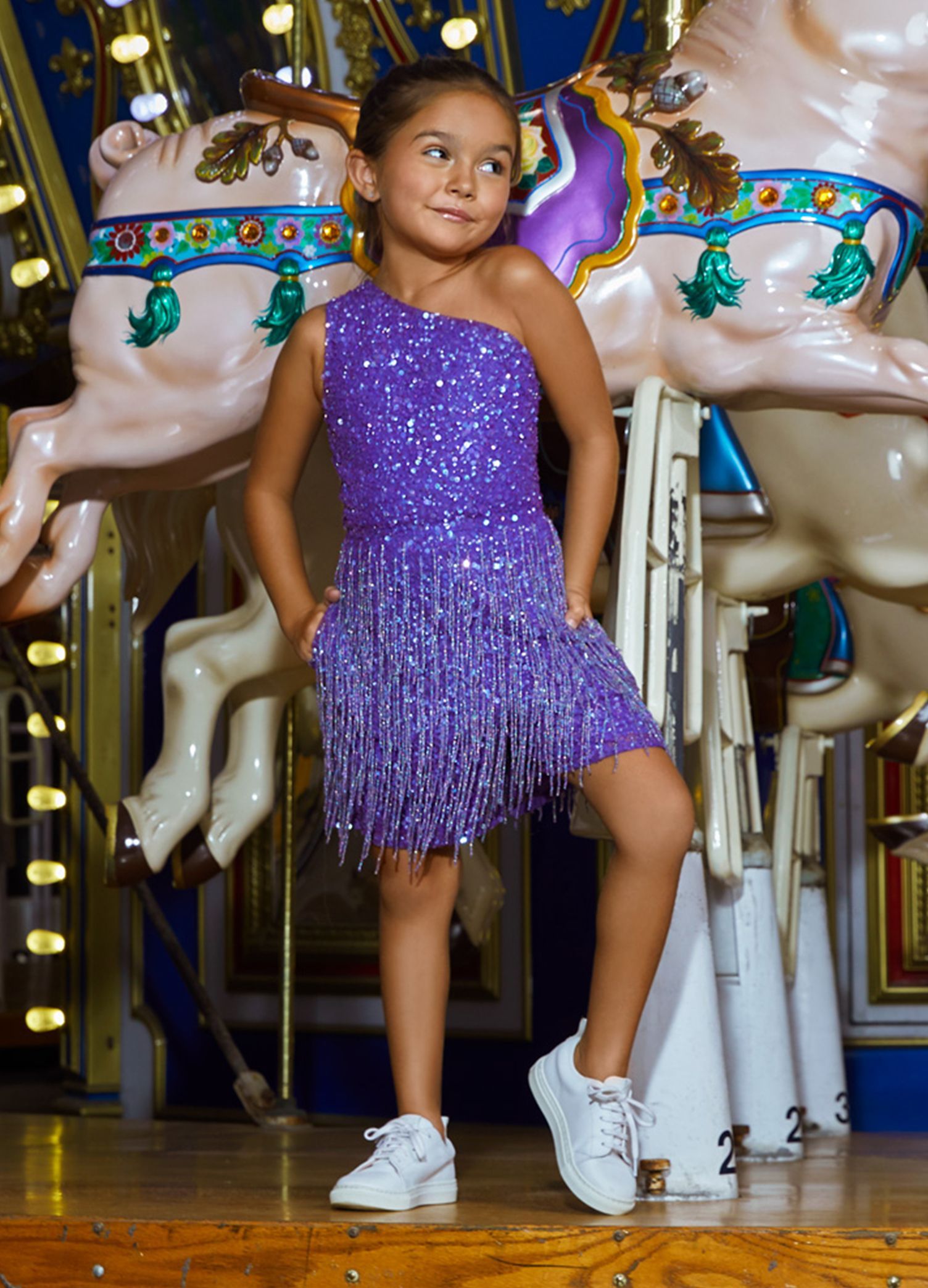 Ashley Lauren 8049 Fun in fringe! This hand-bead sequin kids romper features a one shoulder bustier and layers of fringe throughout the shorts. Excellent fun fashion for your next pageant or special event.  Colors  Iridescent Purple, Iridescent Red, Iridescent Aqua  Sizes  2, 4, 6, 8, 10, 12, 14, 16  Romper One Shoulder Fully Hand Beaded Fringe Pockets