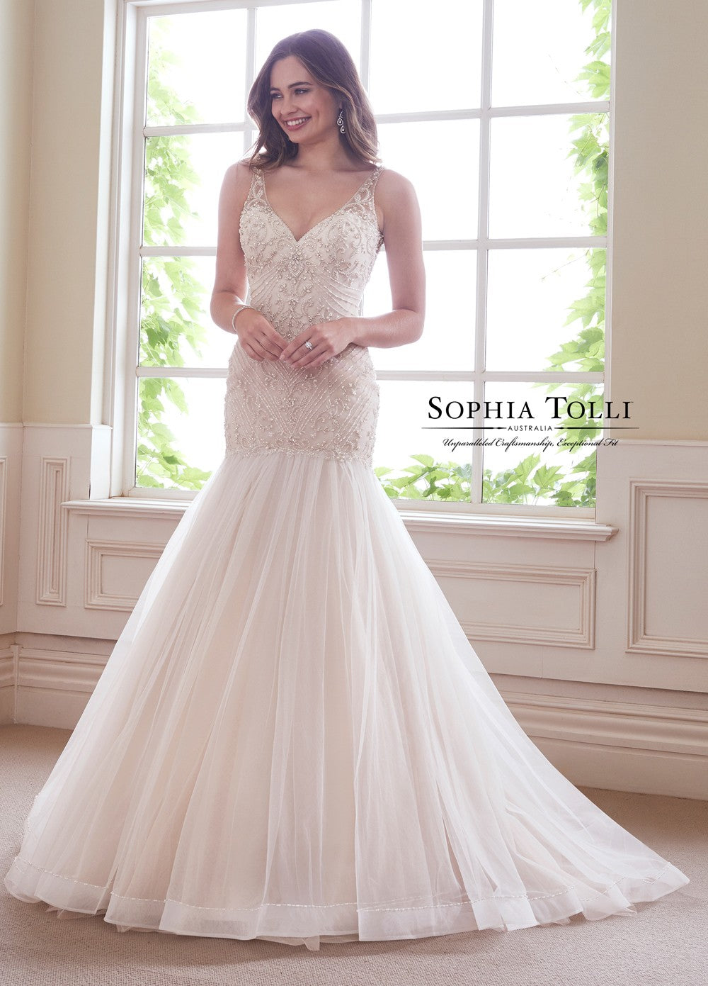 Sophia Tolli Y21811 KYANITE This Sophia Tolli Y 21811 Kyanite trumpet-style wedding gown has an intricately beaded bodice, with illusion straps edging the V-neckline and open scoop back. The gathered tulle skirt begins on the drop waist, and flows to a beaded horsehair hem and chapel train. Diamante buttons trim the back zipper closure. 